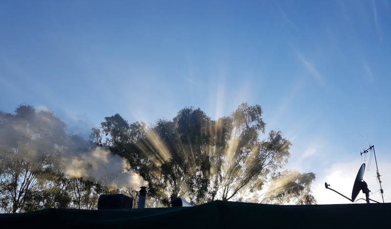 Roof with satellite dish and antenna in shadow against sunrays filtering through tree branches